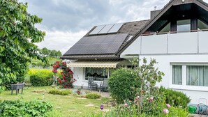Ein modernes Haus mit Satteldach, Solaranlage, überdachter Terrasse und Garten mit verschiedenen Pflanzen und Blumen.