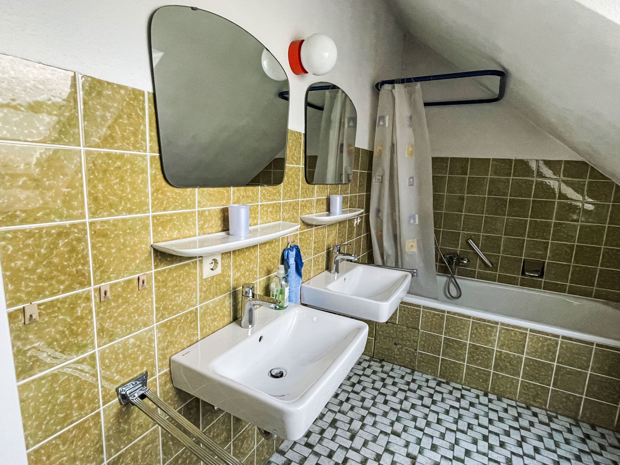 Ein kleines Badezimmer mit zwei Waschbecken, einem Spiegel, einem Handtuchhalter und einer Duschkabine.