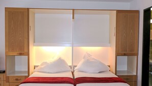 A double bed with white bedding and a red blanket, flanked by wooden cabinets with open shelves. - Pasadena by Interhome (Zermatt)