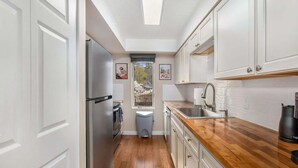 Une cuisine étroite avec des meubles blancs, un plan de travail en bois et une vue par la fenêtre.