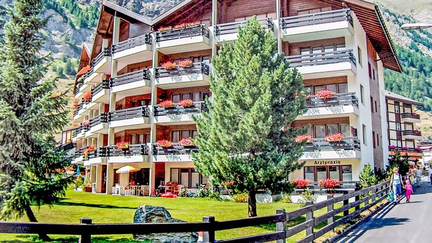 A multi-story hotel with balconies, a garden, and a mountainous backdrop. - Pasadena by Interhome (Zermatt)