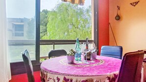 A dining area with a round table covered by a pink tablecloth, chairs, a potted plant, and a window with a view of greenery. - Jardin D'Azur by Interhome (Six Fours La Coudoulière)