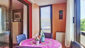 A dining area with a round table covered in a floral tablecloth, surrounded by chairs. There are bottles and glasses on the table, and a window with blinds in the background. - Jardin D'Azur by Interhome (Six Fours La Coudoulière)