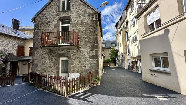 Eine schmale Gasse mit Steinbauten, einem Holzzaun und einem wolkenlosen Himmel.