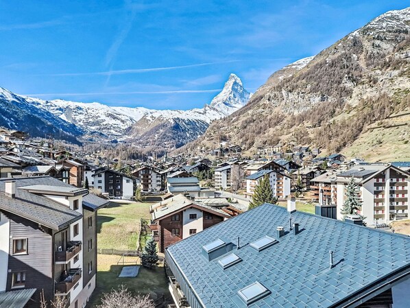 Eine Bergstadt mit schneebedeckten Gipfeln im Hintergrund, moderne Gebäude mit Balkonen und einem klaren Himmel.