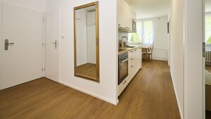 A modern kitchen with white cabinets, a built-in oven, and a window with sheer curtains. - Forest line by Interhome (Josefuv Dul)