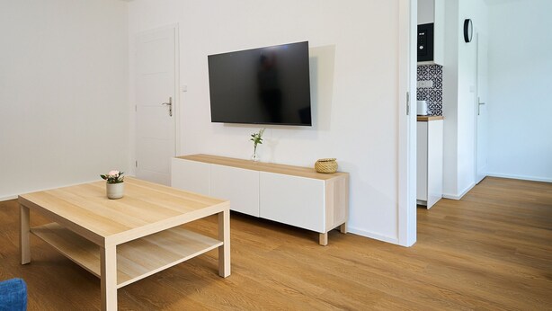 A modern living room with a wooden table, a TV mounted on the wall, and a white cabinet. - Forest line by Interhome (Josefuv Dul)