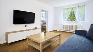 A modern living room with a flat-screen TV, a wooden coffee table, a blue sofa, and a window with sheer curtains. - Forest line by Interhome (Josefuv Dul)