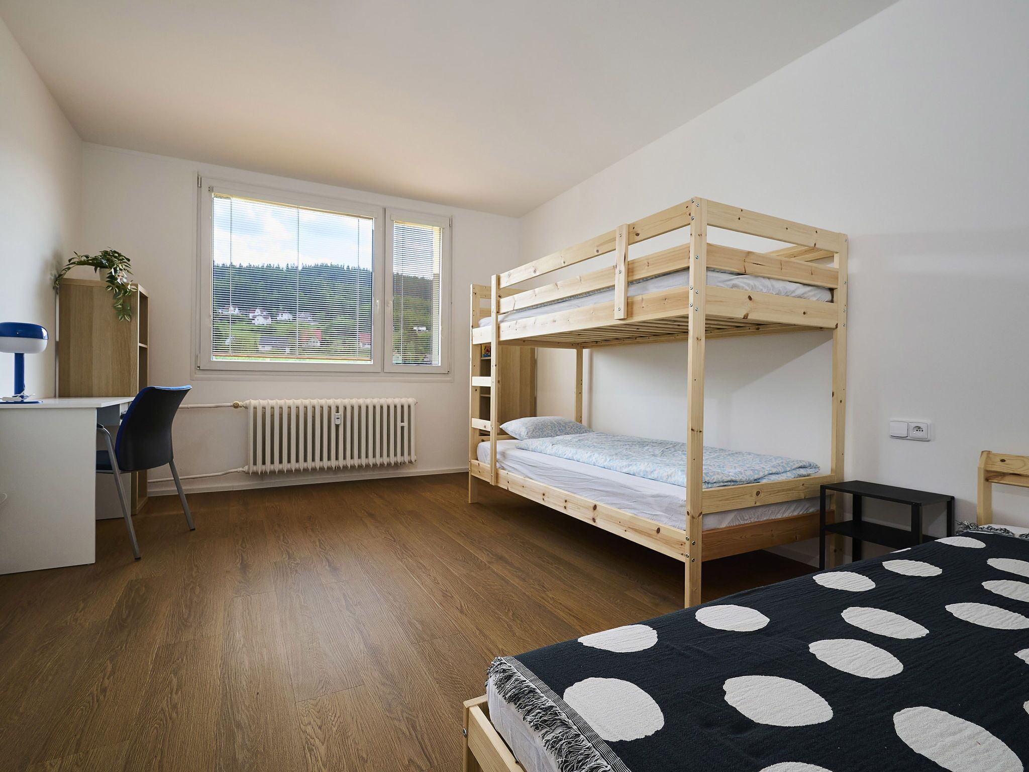 A bunk bed room with a desk and chair, a radiator, and a window with blinds.
