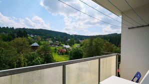 A balcony with a view of a village, a white table, and blue chairs. - Forest line by Interhome (Josefuv Dul)