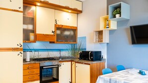 A compact kitchen with wooden cabinets, a built-in oven, and a microwave. There's a small dining area with a table and chairs. - casa Peggy by Interhome (Santo Stefano al Mare)