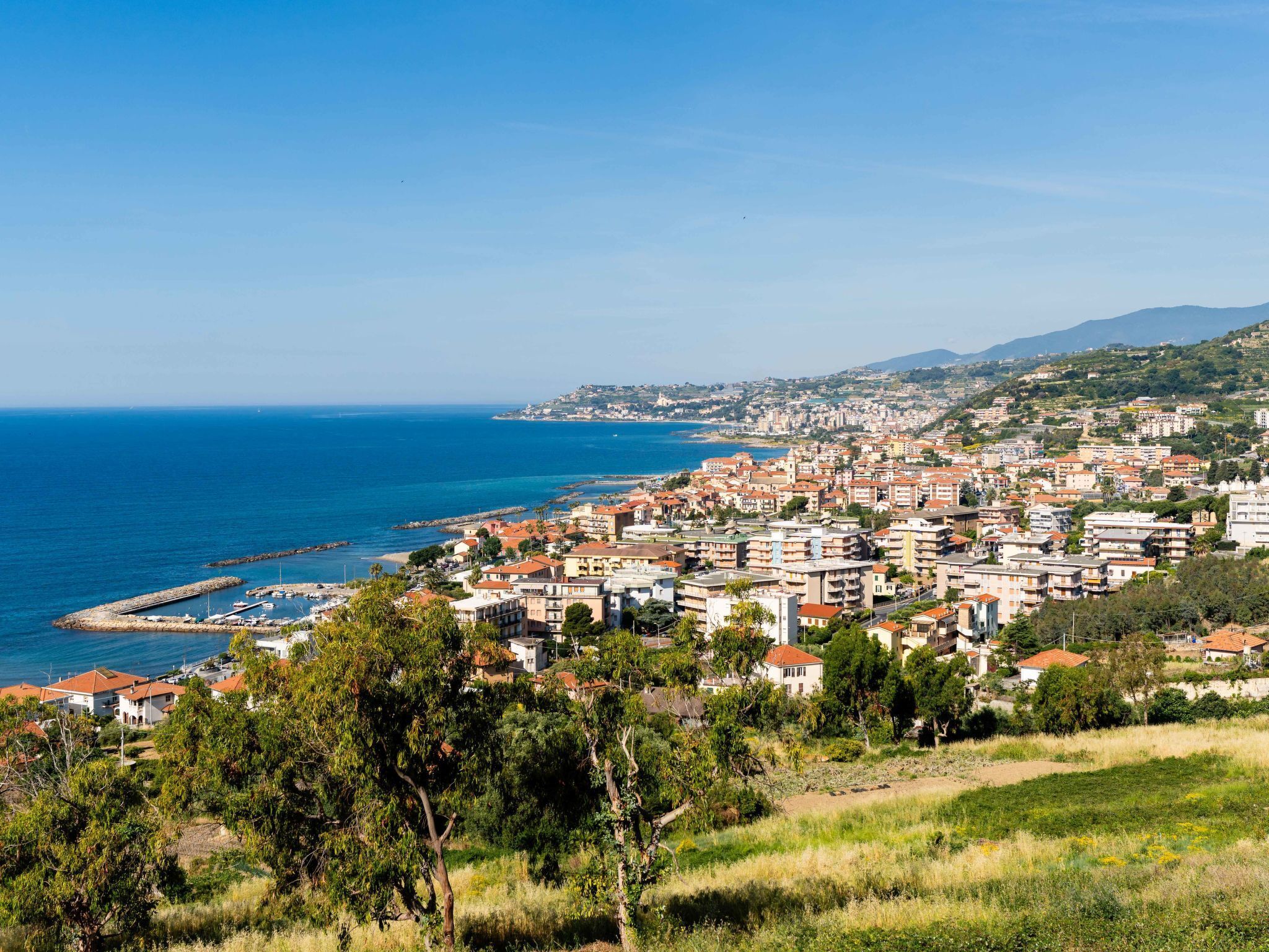 Un pueblo costero con un puerto deportivo, edificios residenciales y un paisaje montañoso de fondo.