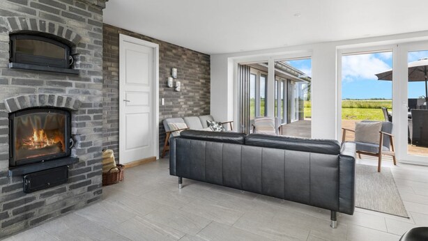 A modern living room with a stone fireplace, a leather sofa, and a large sliding glass door leading to an outdoor patio. - "Ung" - 460m from the sea by Interhome (Otterup)