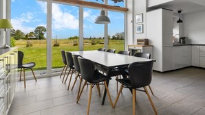 A modern kitchen with large windows, a dining area with a white table and black chairs, and a view of the countryside. - "Ung" - 460m from the sea by Interhome (Otterup)