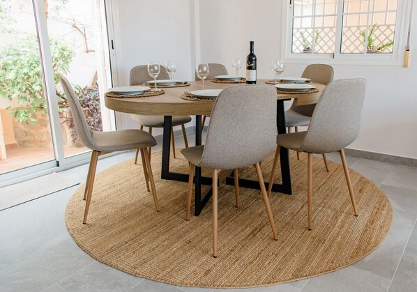 A dining area with a round table, six chairs, and a bottle of wine.