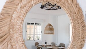 A round mirror with a woven frame reflecting a dining area with a table, chairs, and a hanging light fixture. - Villa, 3 Terraces, 5-Min Walk to Burriana Beach (Nerja)