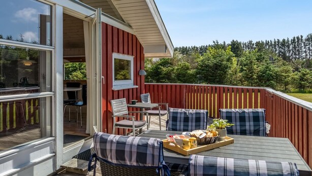 An outdoor deck with a dining area, including a table with a tray of food, two chairs, and a bench.