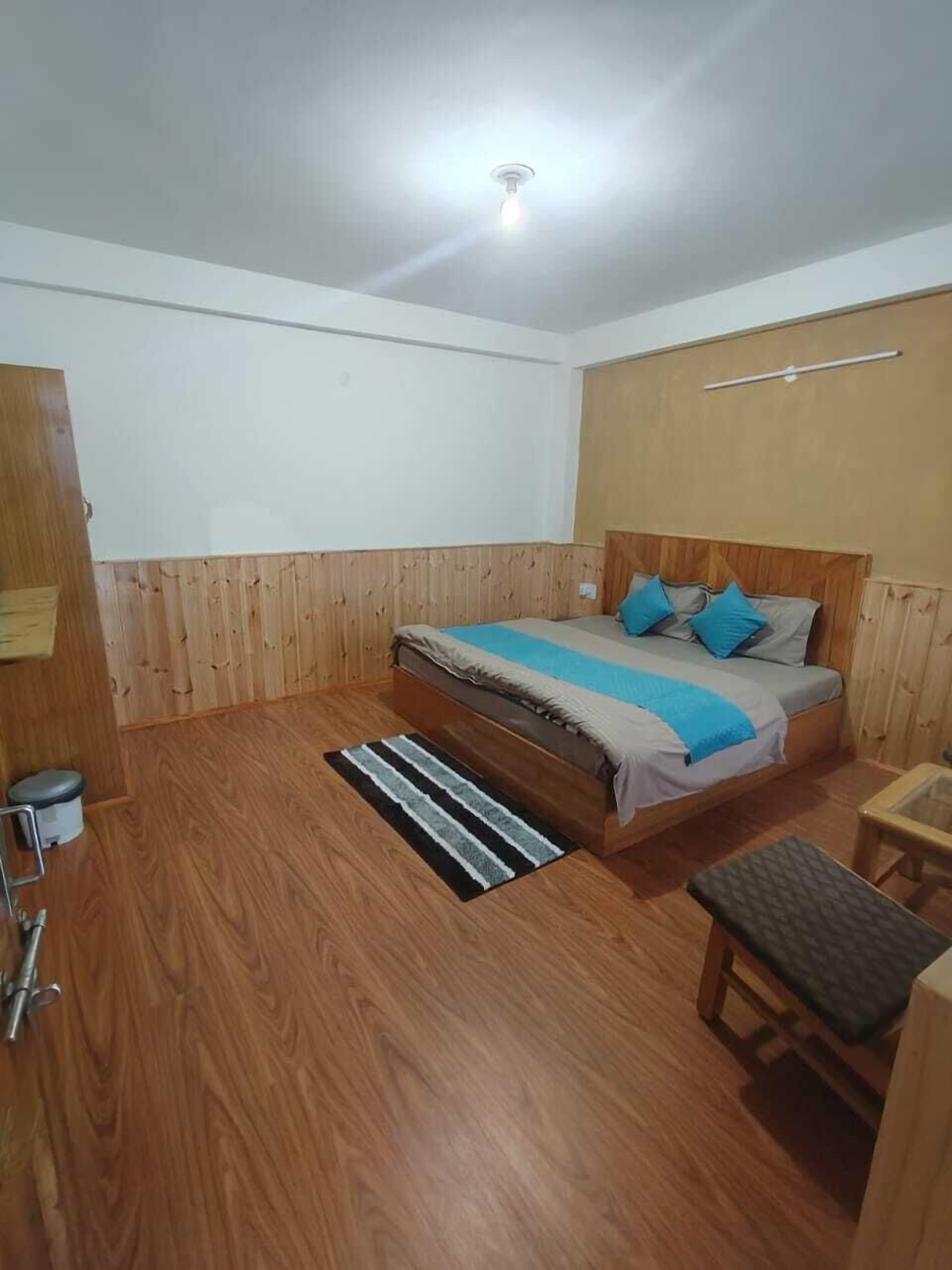 A bedroom with a wooden bed, a small bedside table, a bench, and a wooden floor.