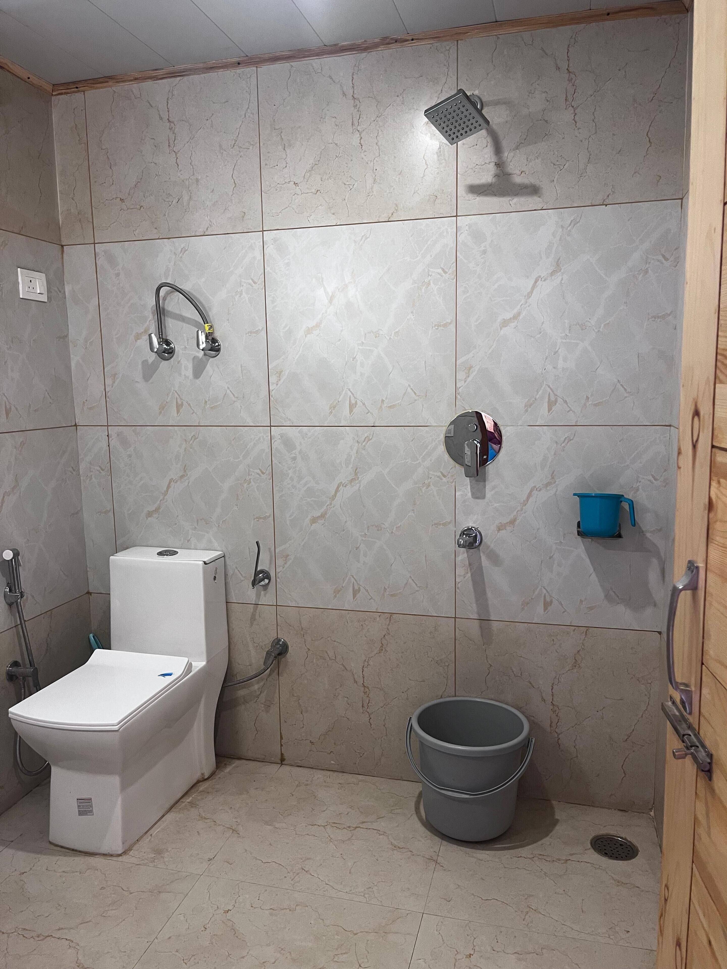 A bathroom with a toilet, shower, and bucket.