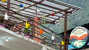Un hôtel avec une enseigne indiquant « Greenwoods Old Manali Hotel & Cafe », un escalier et une moto garée à l’extérieur.