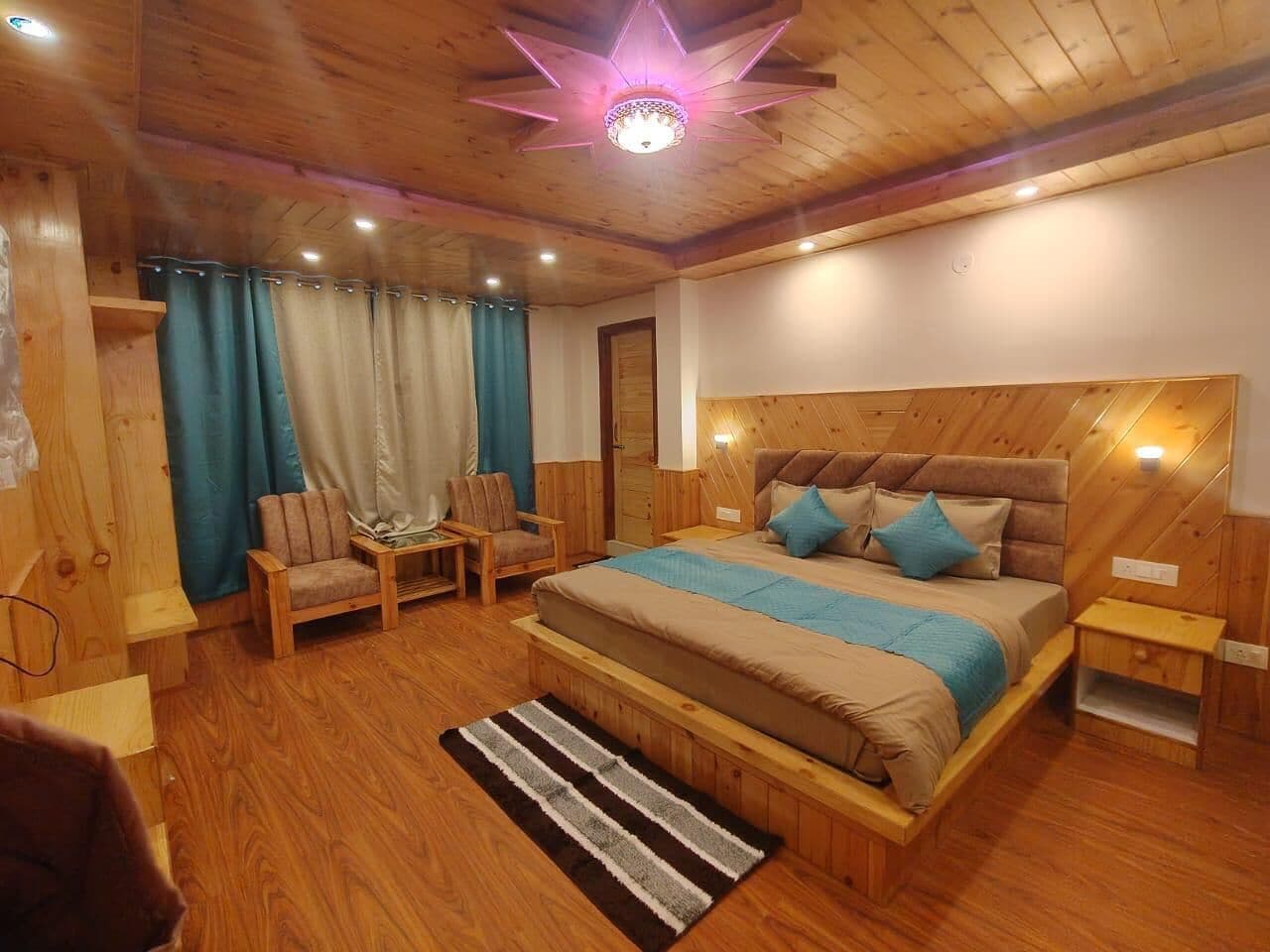 A wooden-floored bedroom with a bed, two chairs, a nightstand, and a star-shaped ceiling light.