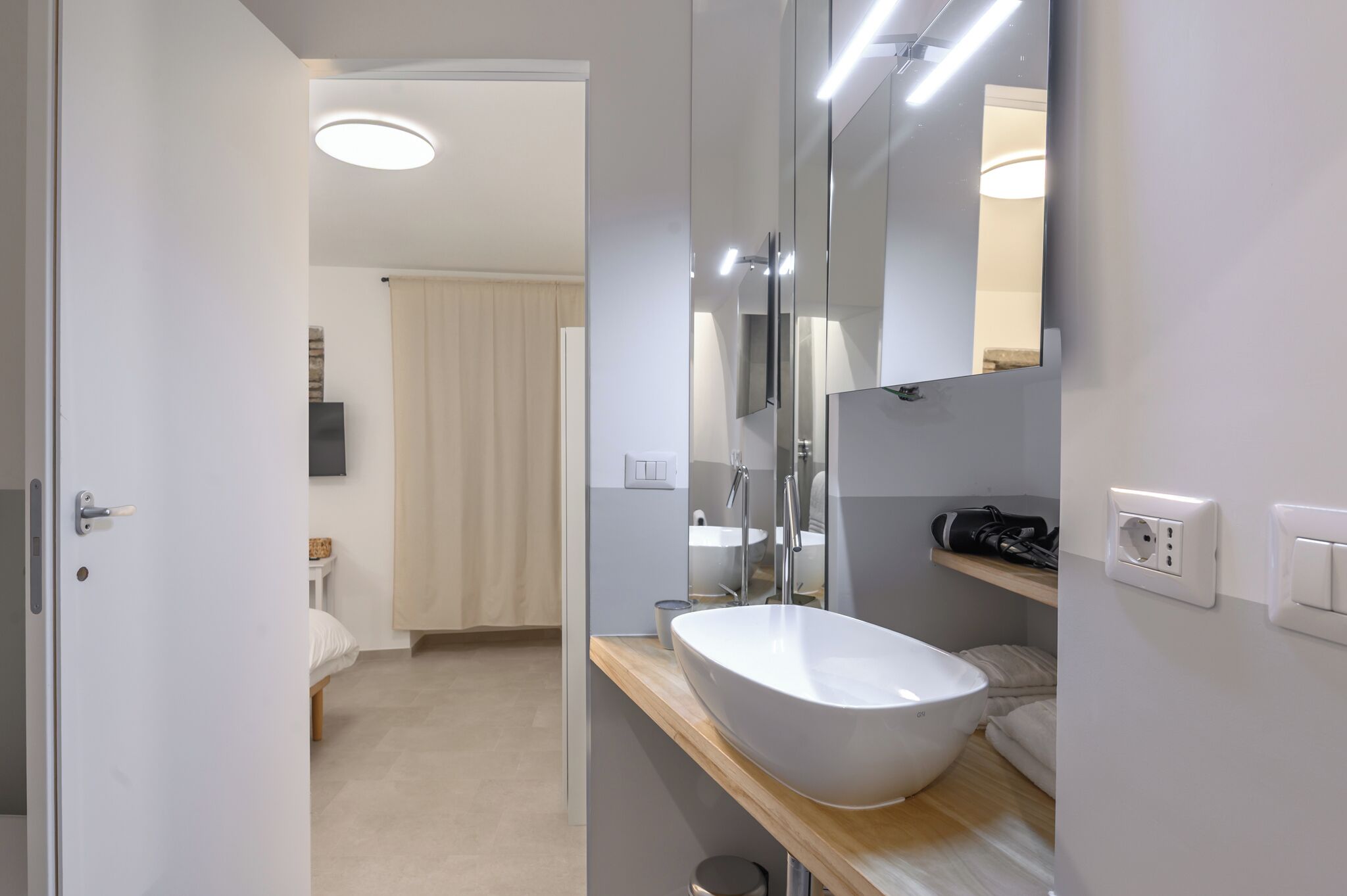 A modern bathroom with a large mirror, a white sink, and a shower area.