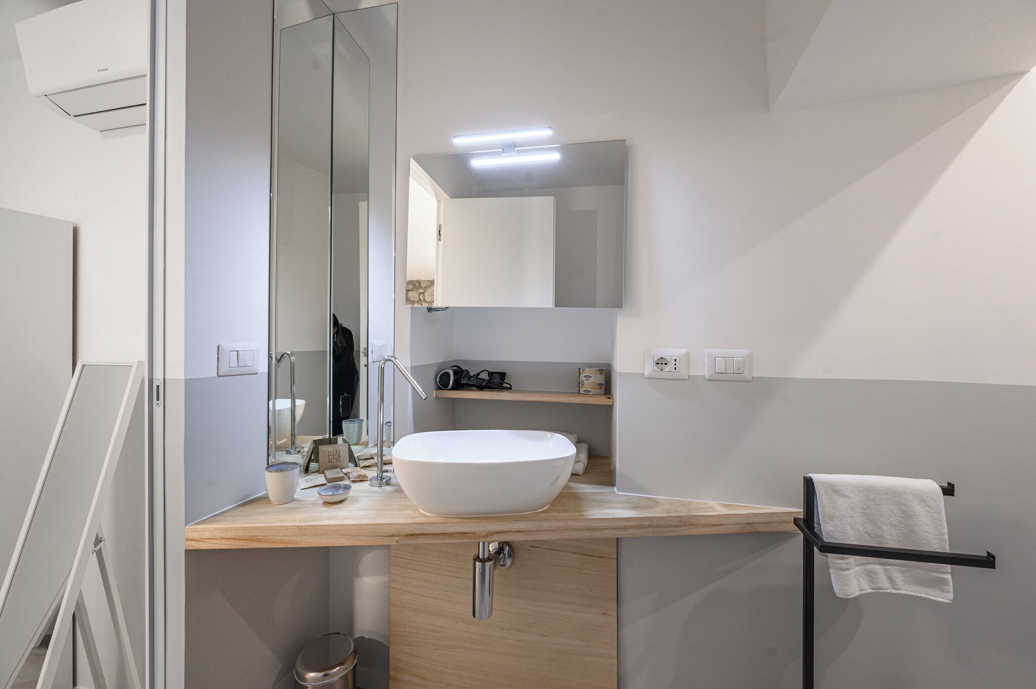 A modern bathroom with a large mirror, a white vessel sink, a towel rack, and a wooden vanity.