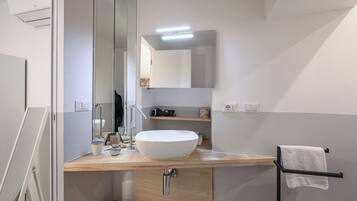 A modern bathroom with a large mirror, a white vessel sink, a towel rack, and a wooden vanity.