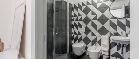 A modern bathroom with a glass shower enclosure, a toilet, bidet, and a sink with a mirror.