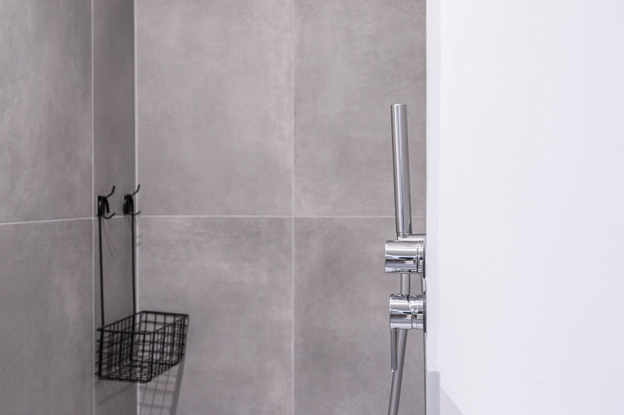 A modern bathroom with a chrome showerhead and a black wire basket on the wall.