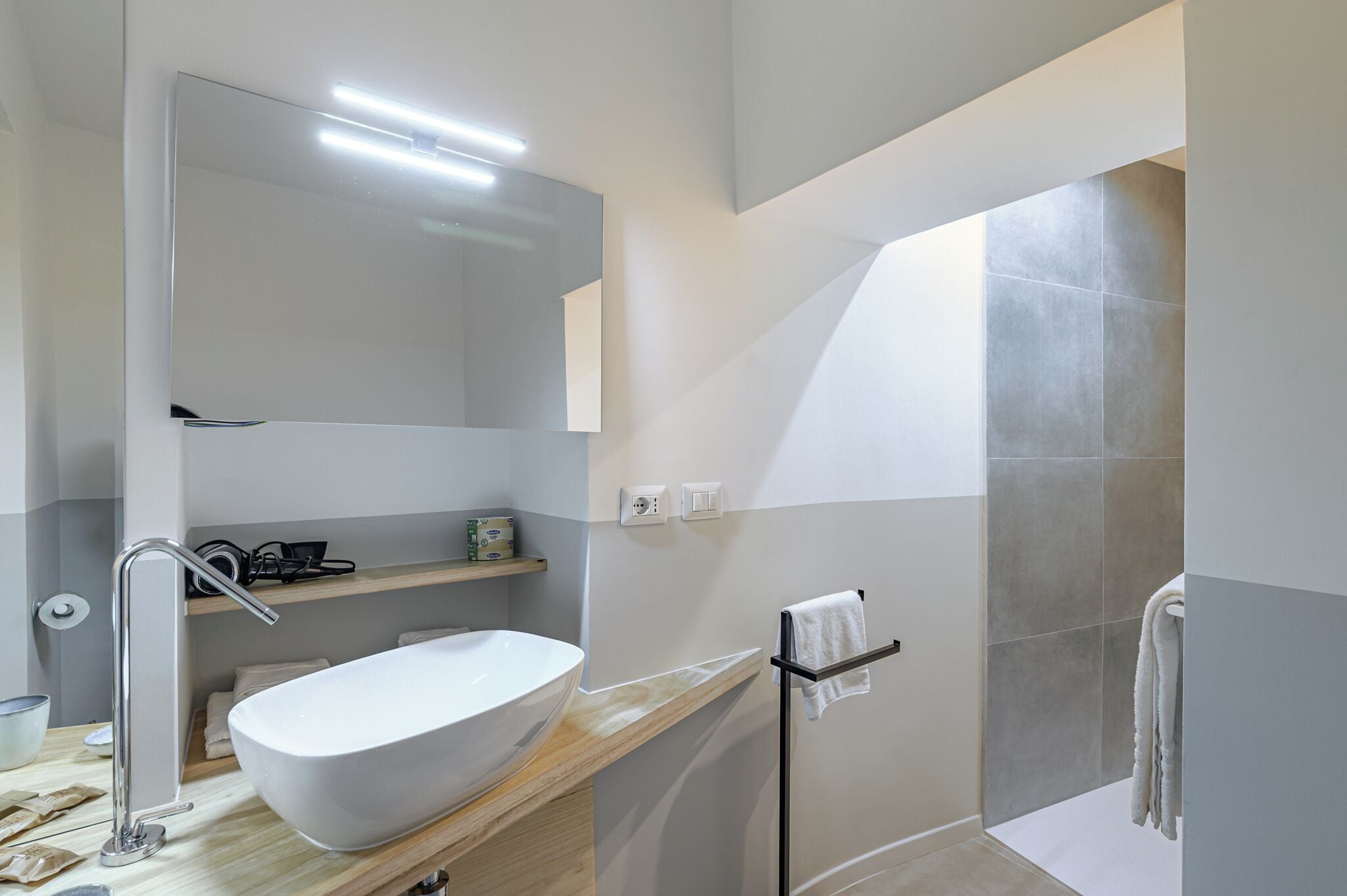 Un baño moderno con un lavabo blanco grande, un espejo y una zona de ducha.