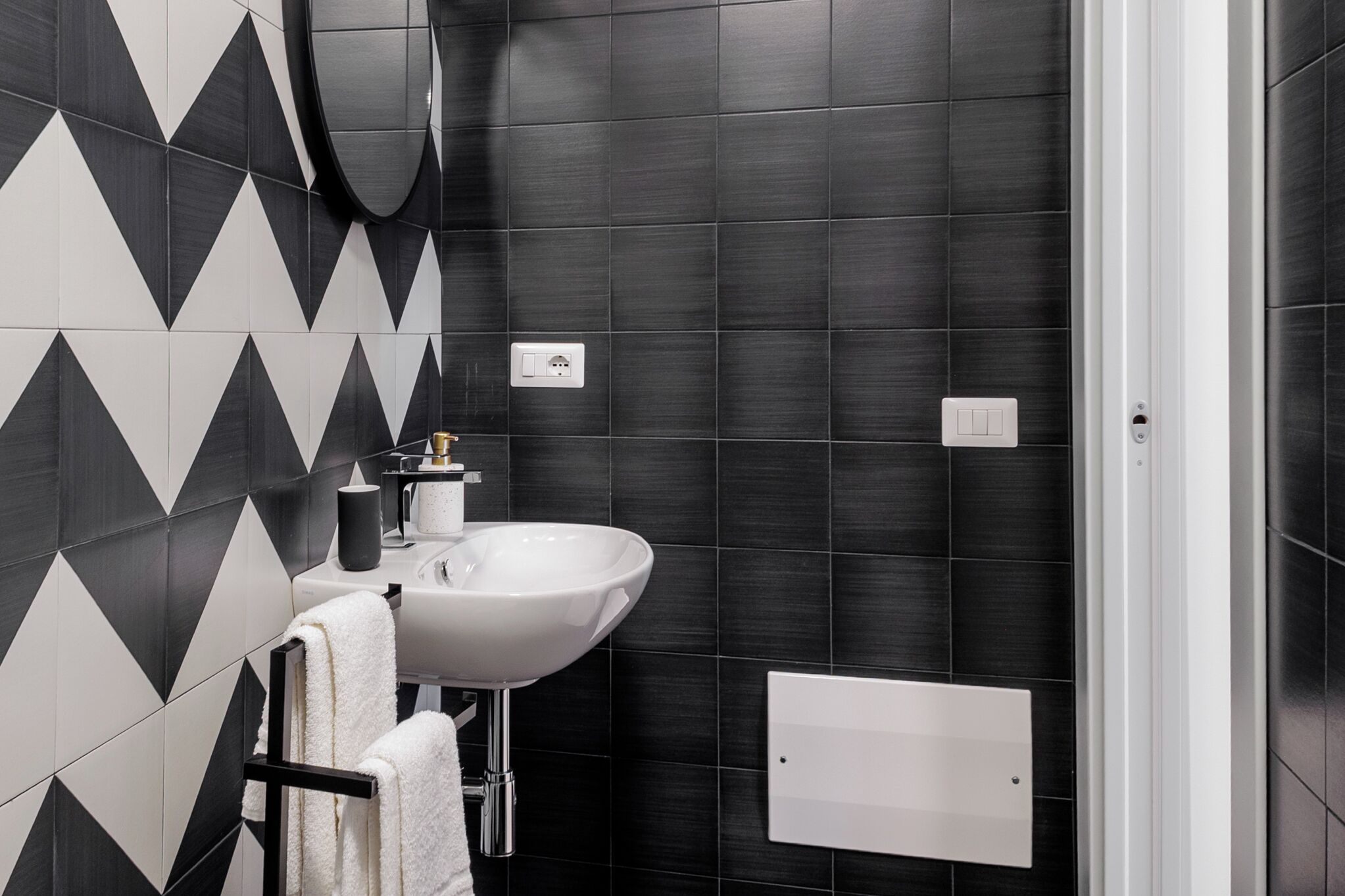 Un bagno moderno con piastrelle a motivi bianchi e neri, un lavandino bianco e un porta asciugamani.