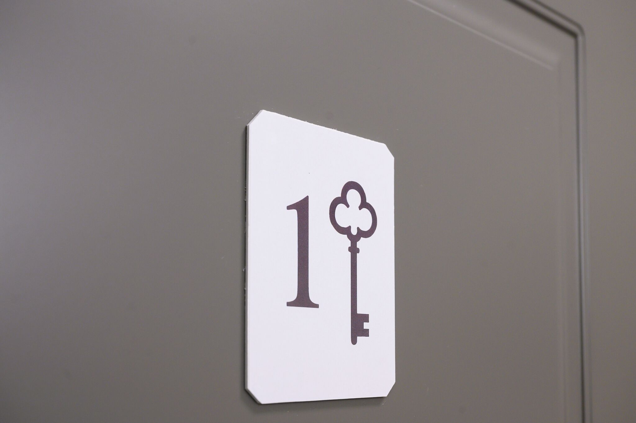 A white sign with the number 1 and a key symbol on a grey wall.