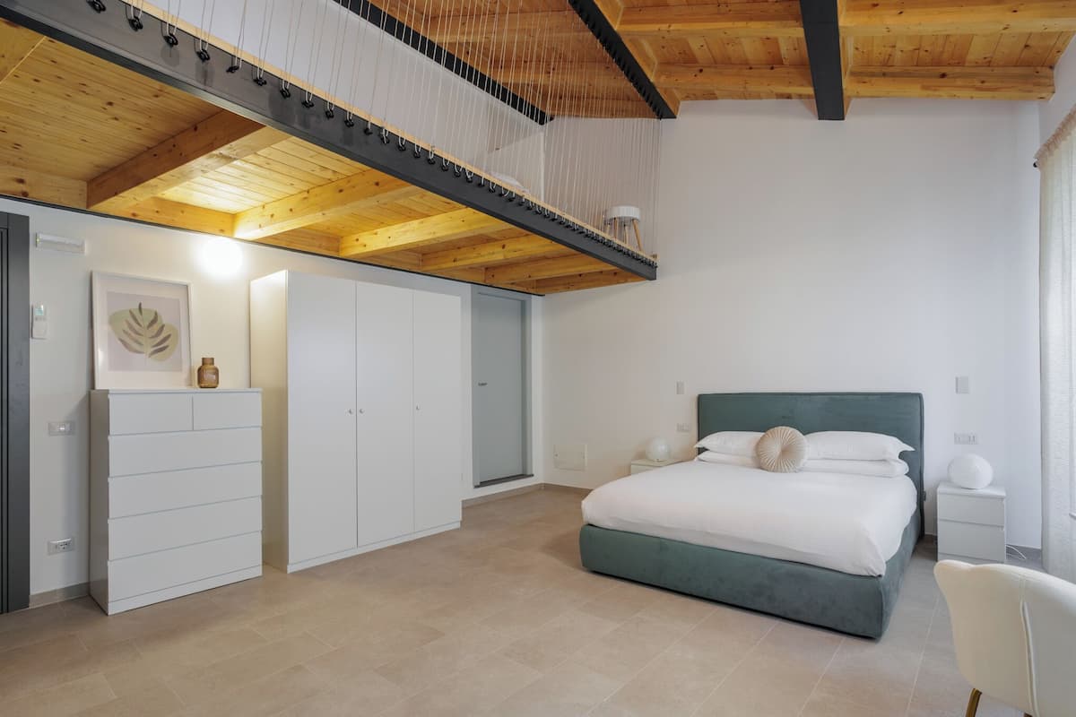 Un dormitori modern amb llit, una commode, un armari i un sostre amb bigues al descobert.