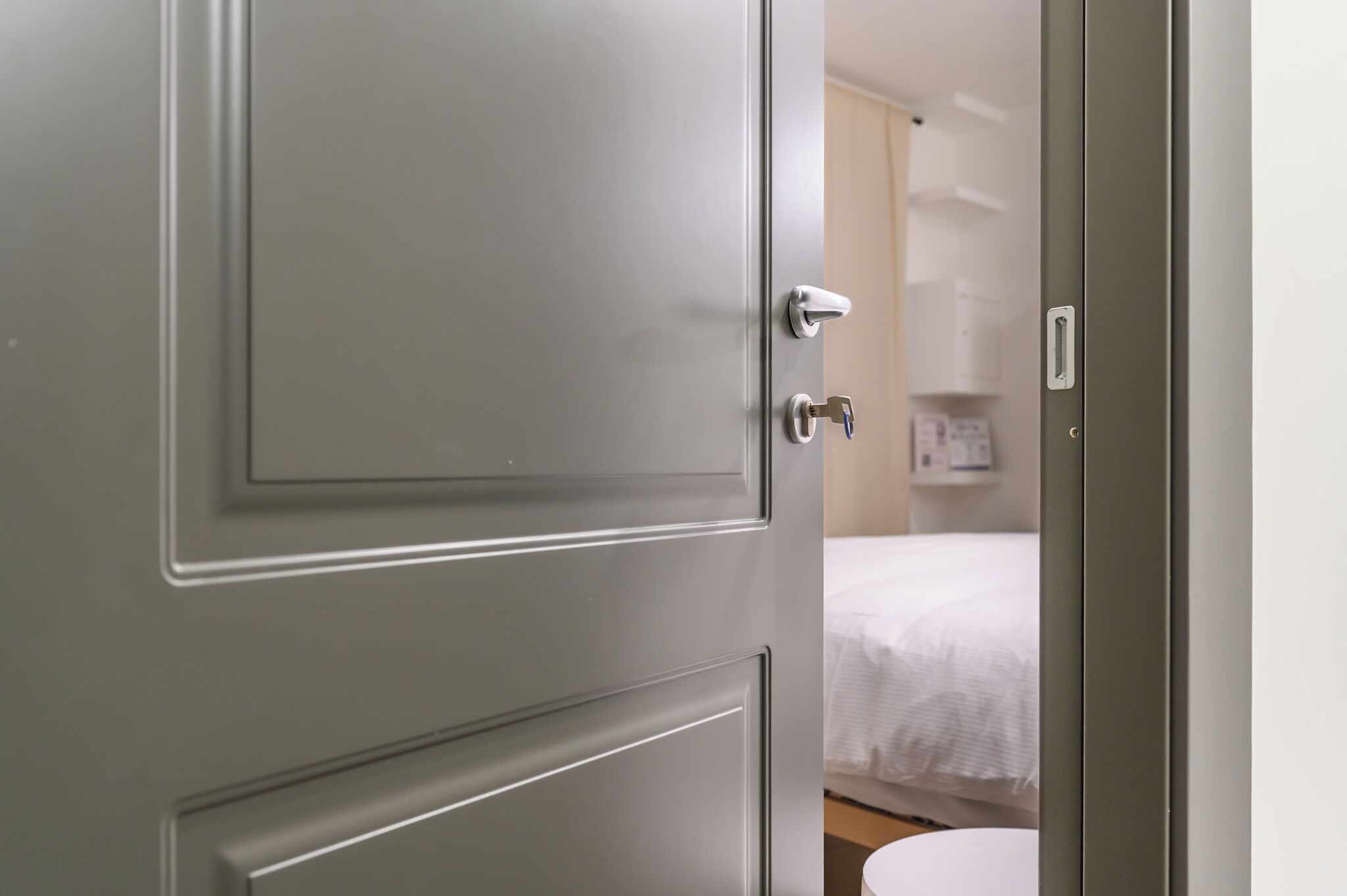A closed door with a handle and a keyhole, leading to a room with a bed and a white wall.