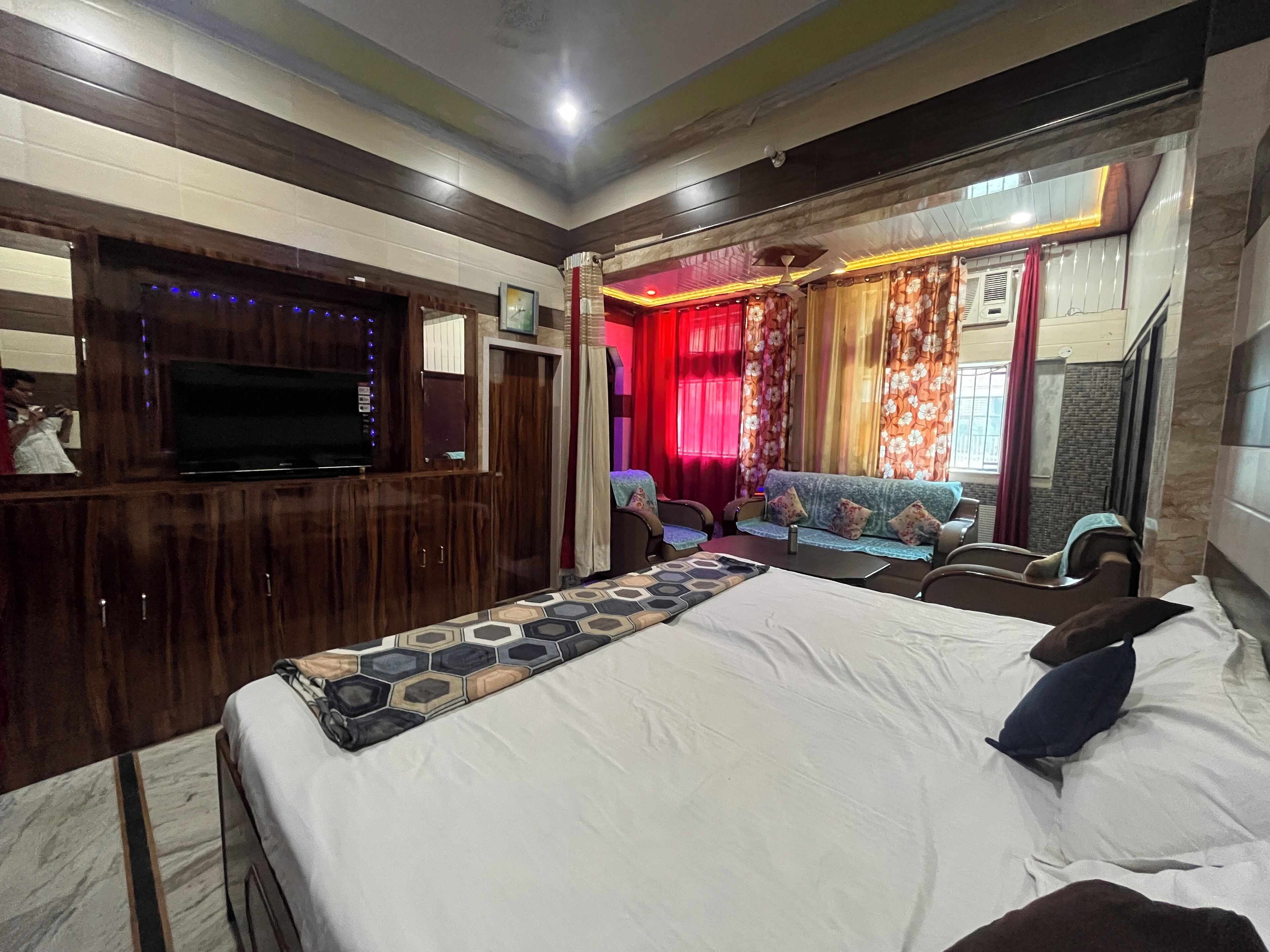 A hotel room with a large bed, a sofa, a TV, and a ceiling fan.
