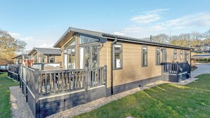 Ein modernes Mobilheim mit Terrasse, großen Fenstern und Auffahrt mit Kies.
