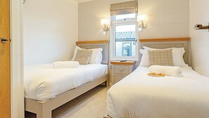 Ein Hotelzimmer mit zwei Betten, einem Fenster mit Jalousien, einem Nachttisch und einer Lampe.