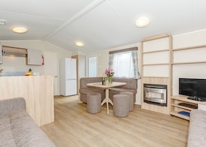 A compact living space with a kitchenette, a dining area with a table and chairs, a seating area with ottomans, a television, and a fireplace.