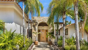 Un patio con un arco de piedra que conduce a una puerta de madera, rodeado de palmeras y plantas en macetas.