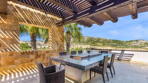 Un patio al aire libre con un muro de piedra, una pérgola de madera y vistas al paisaje costero.