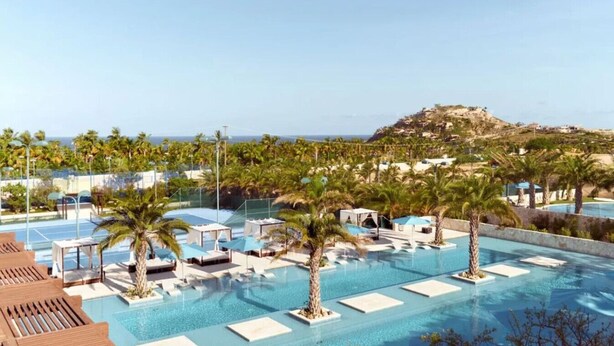 Una piscina infinita en la azotea con sillones de descanso y palmeras, con vistas a un paisaje costero.