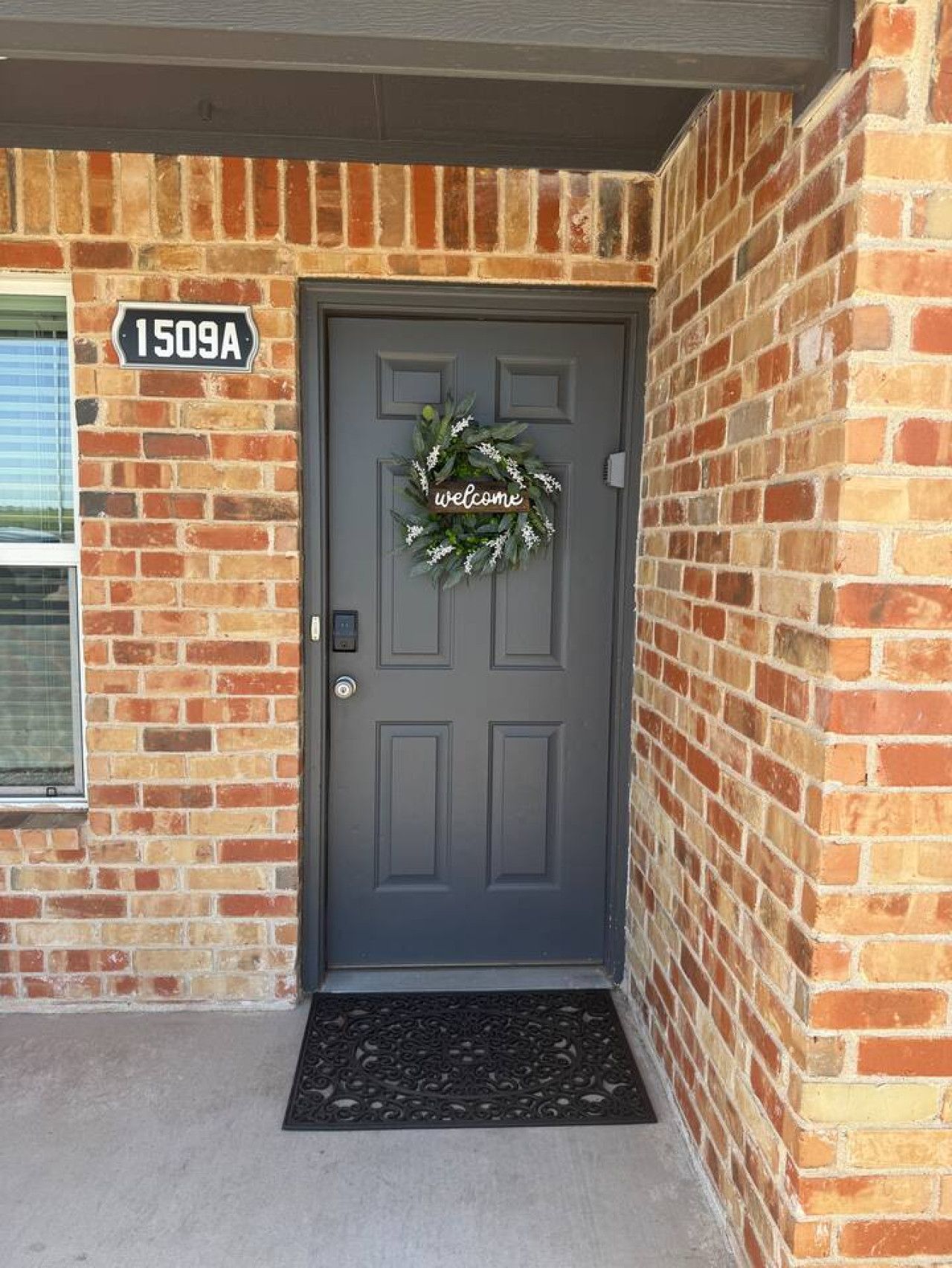 A residential front door with a welcome wreath, a mailbox, and a house number sign.