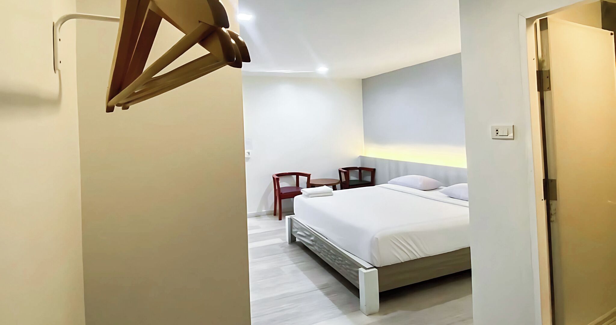 Habitación de hotel con una cama, dos sillas, una mesita y una silla de madera apoyada contra la pared.