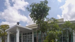 Een modern gebouw met een overdekt terras, omringd door groen en een bord met Thaise letters.