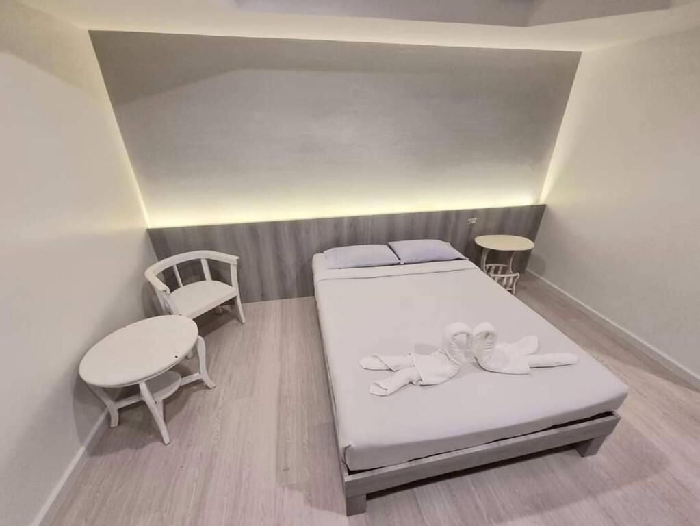 A modern hotel room with a bed, two white chairs, and a small round table.