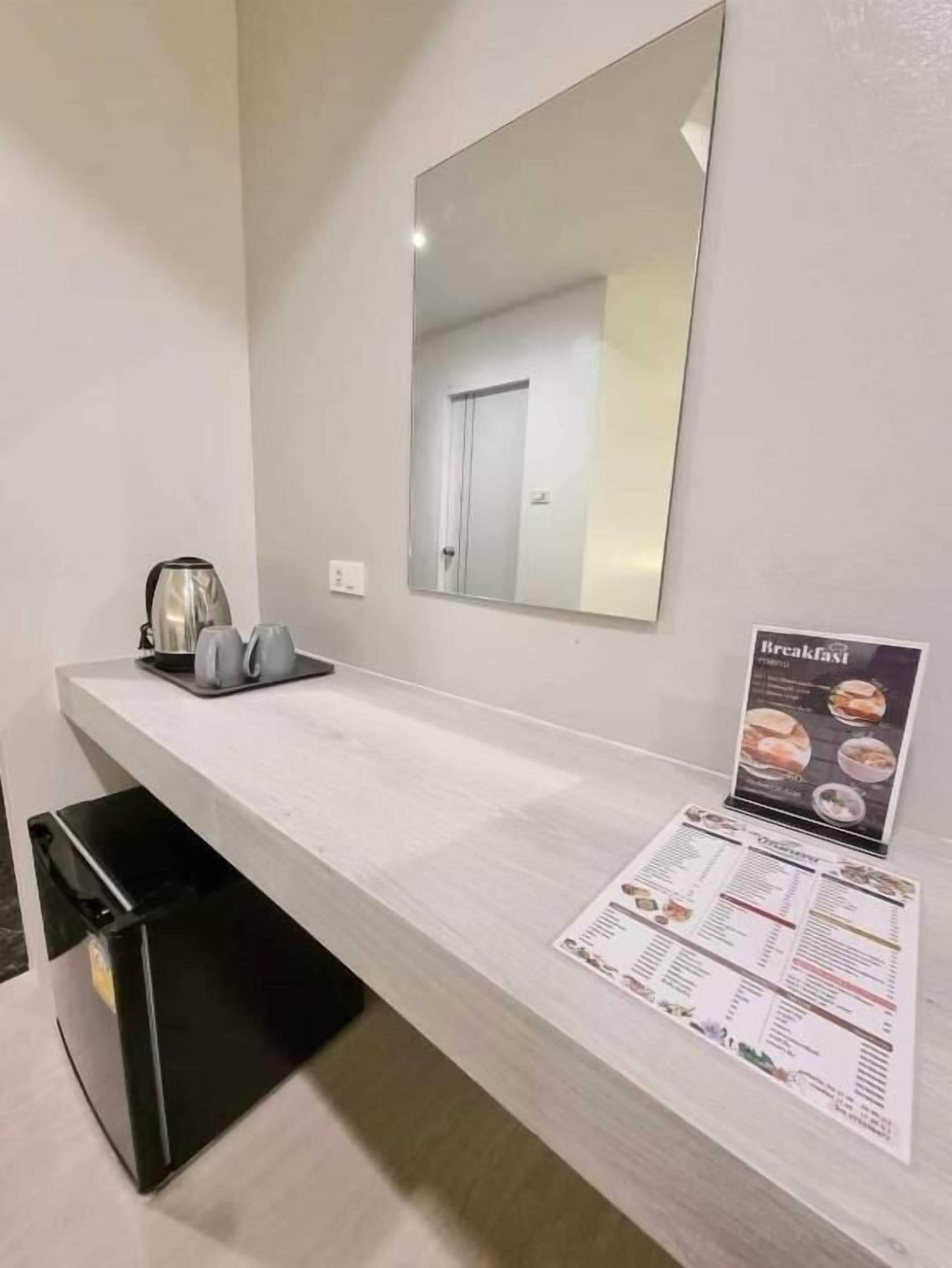 A modern kitchen with a white countertop, a kettle, a coffee maker, and a breakfast menu sign.
