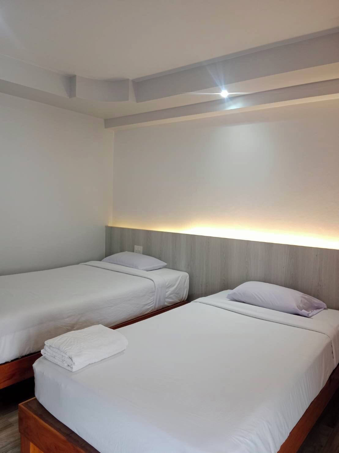 Habitación de hotel con dos camas individuales, cabecera de madera y una lámpara en el techo.