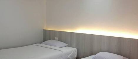 Habitación de hotel con dos camas individuales, cabecera de madera y una lámpara en el techo.