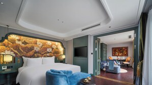 Une chambre d’hôtel avec un grand lit, un fauteuil bleu, une table ronde et une tête de lit décorative.
